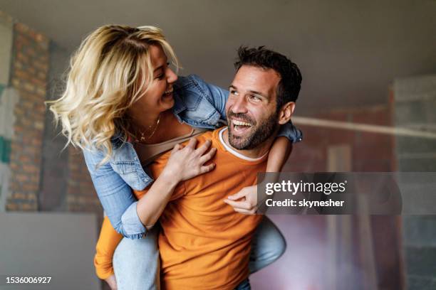 carefree couple having fun while piggybacking at construction site. - piggyback stock pictures, royalty-free photos & images