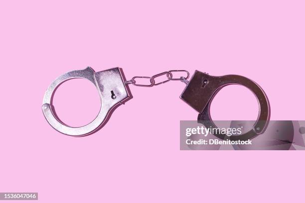 closed metal handcuffs on a pink background. police, prison, jail, prisoner, illegal, robbery, law, trial and thief concept. - handcuffs imagens e fotografias de stock