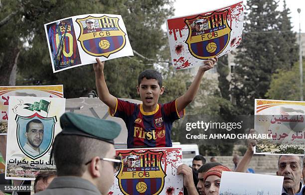 Palestinian boy wearing an FC Barcelona football club's T-shirt holds up placards, bearing a portrait of Israeli soldier Gilad Shalit on the emblem...