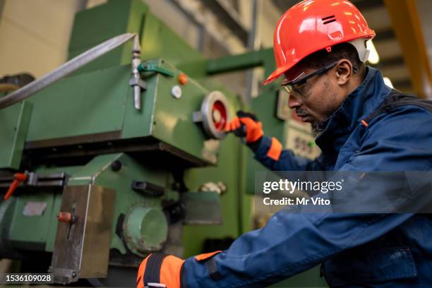 a dark-skinned industrial worker prepares a metalworking machine for work - production line worker stock pictures, royalty-free photos & images