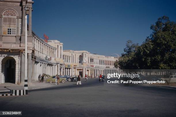 Pedestrians and cyclists pass cars parked on Connaught Place in the central business district of New Delhi, India circa 1960. Designed by English...