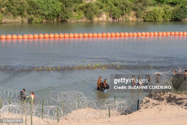 Migrants walk by a string of buoys placed on the water along the Rio Grande border with Mexico in Eagle Pass, Texas, on July 16, 2023. The buoy...