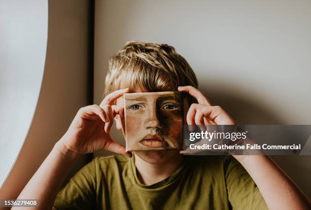 a little boy holds a small oil painting of himself over his face - children art show stock pictures, royalty-free photos & images