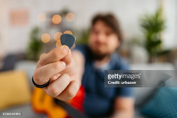 young man holding up a plectrum for a guitar at home - gitaarplectrum stockfoto's en -beelden