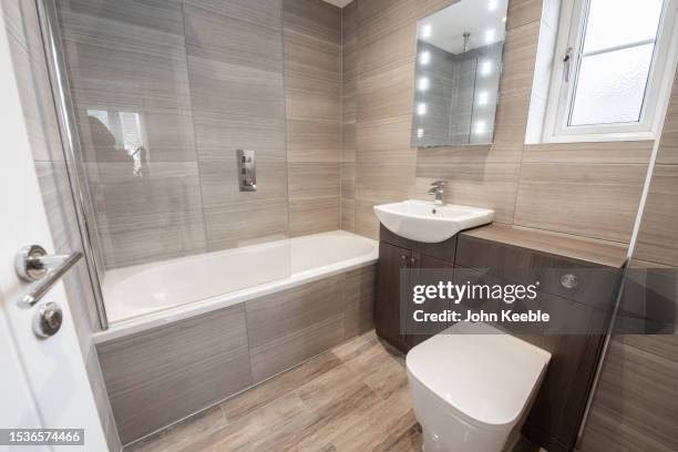 property interior of a general interior view of a grey, brown tiled bathroom en-suite with white suite, bath, sink fitted to a vanity cabinet, toilet, mirror with led lights, tiled wood effect floor, chrome taps, - tawny stock pictures, royalty-free photos & images