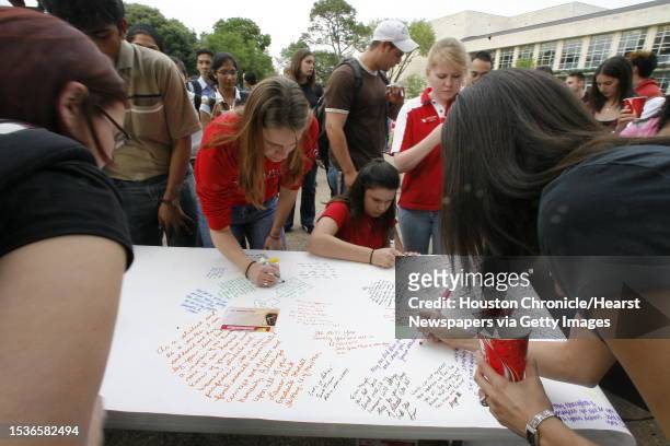 Students at the U of H candlelight vigil, including Emily Swank and Kelli McDonald, sign and write notes on a roll of paper which will be sent to...