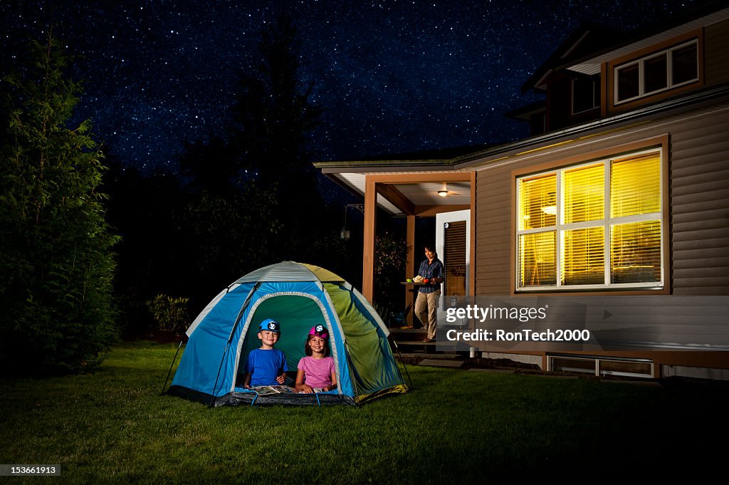 Children camping in a tent in the backyard