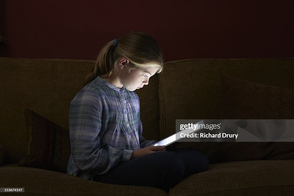 Girl sat on sofa using digital tablet at night