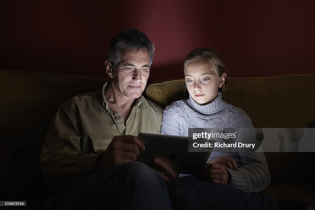 Dad and daughter sat on sofa using digital tablet