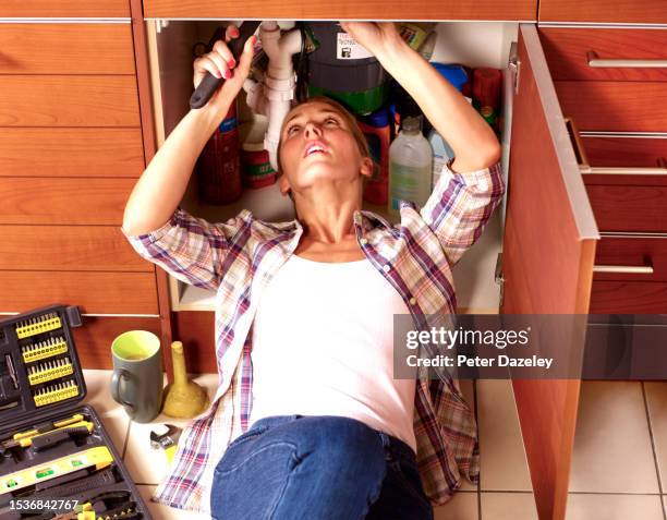 woman plumber under kitchen sink - inconvenience stock pictures, royalty-free photos & images