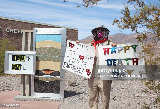 Protestor stands next to a digital display of an unofficial heat reading at Furnace Creek Visitor Center during a heat wave in Death Valley National...