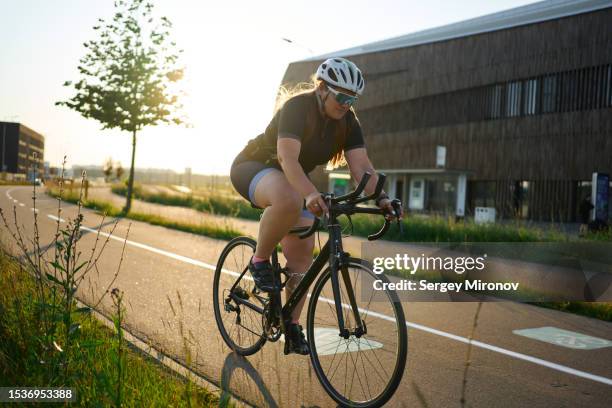 plus size young woman training on bicycle at sunset - action plus general stockfoto's en -beelden