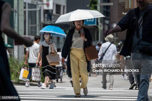 Woman uses an umbrella to shelter from the midday sun as she crosses the street in downtown Tokyo on July 17, 2023. Scorching heat across the...