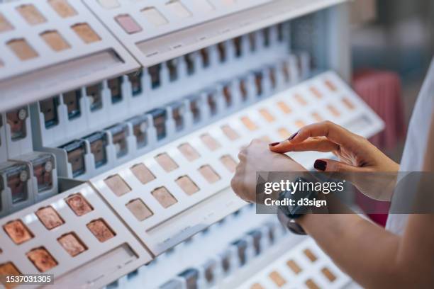 close up of a young woman shopping in a beauty store, applying eye shadow tester on her hand. cosmetics, make-up, beauty products shopping concept - make up grundierung stock-fotos und bilder