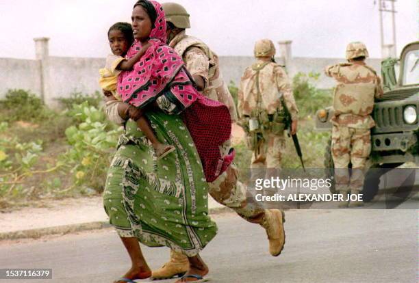 Marine escorts a Somali woman and child to safety 12 June 1993 seconds before a large explosion ripped through one of warlord Mohamed Farrah Aidid's...