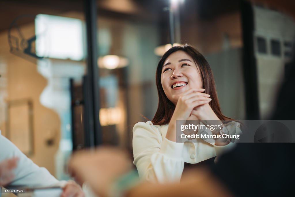 Asian chinese beautiful young woman toothy smile during discussion with team at meeting room