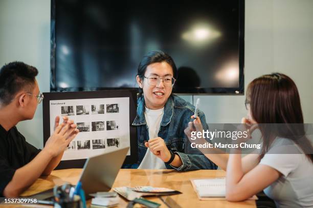 asiático chino guapo sonriente joven adulto dando presentación con el equipo en el estudio de diseño - storyboard fotografías e imágenes de stock