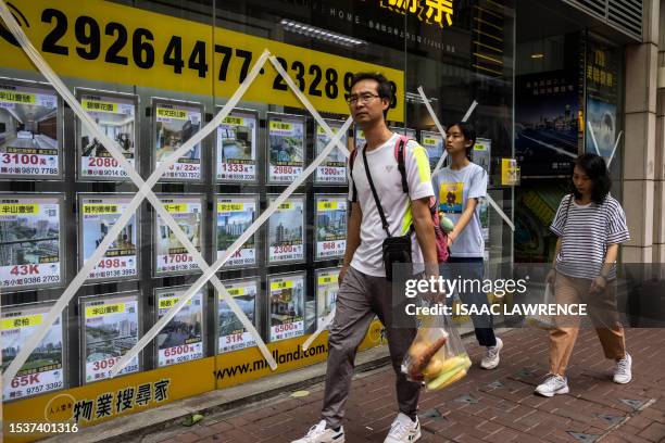 People walk past a store window marked with masking tape as a precaution as Typhoon Talim passes near Hong Kong on July 17, 2023.