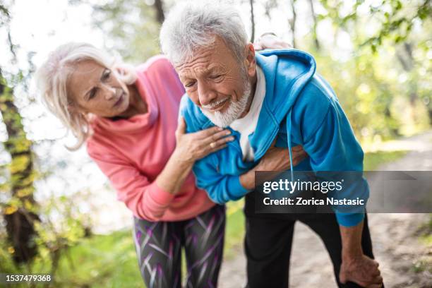 senior man with wife running while having heart problems - cardiovascular disease stockfoto's en -beelden