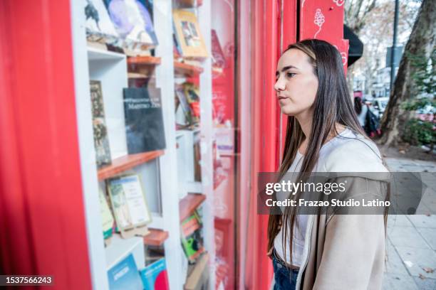 mujer joven busca libros en la vitrina de la biblioteca - biblioteca pública fotografías e imágenes de stock