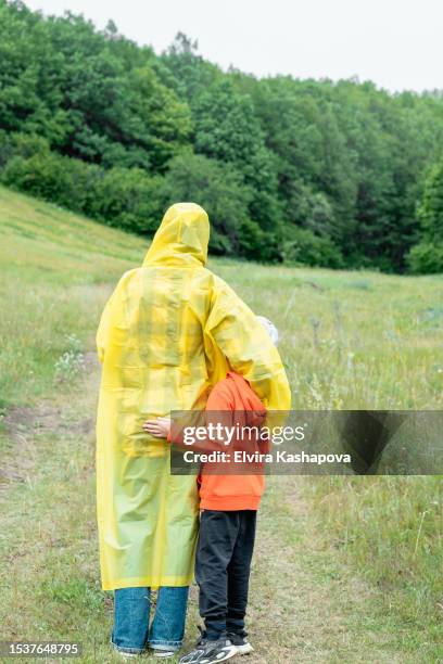 lost in the forest, a young woman with her son in a yellow raincoat stands with her back against the background of the forest. - kapstaden stockfoto's en -beelden