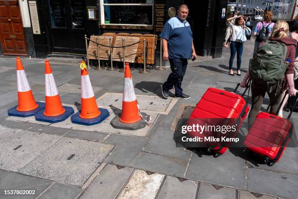 Four traffic cones stand on an uneven surface where maintenance covers make a trip hazard on the pavement as a warning for pedestrians to avoid on...