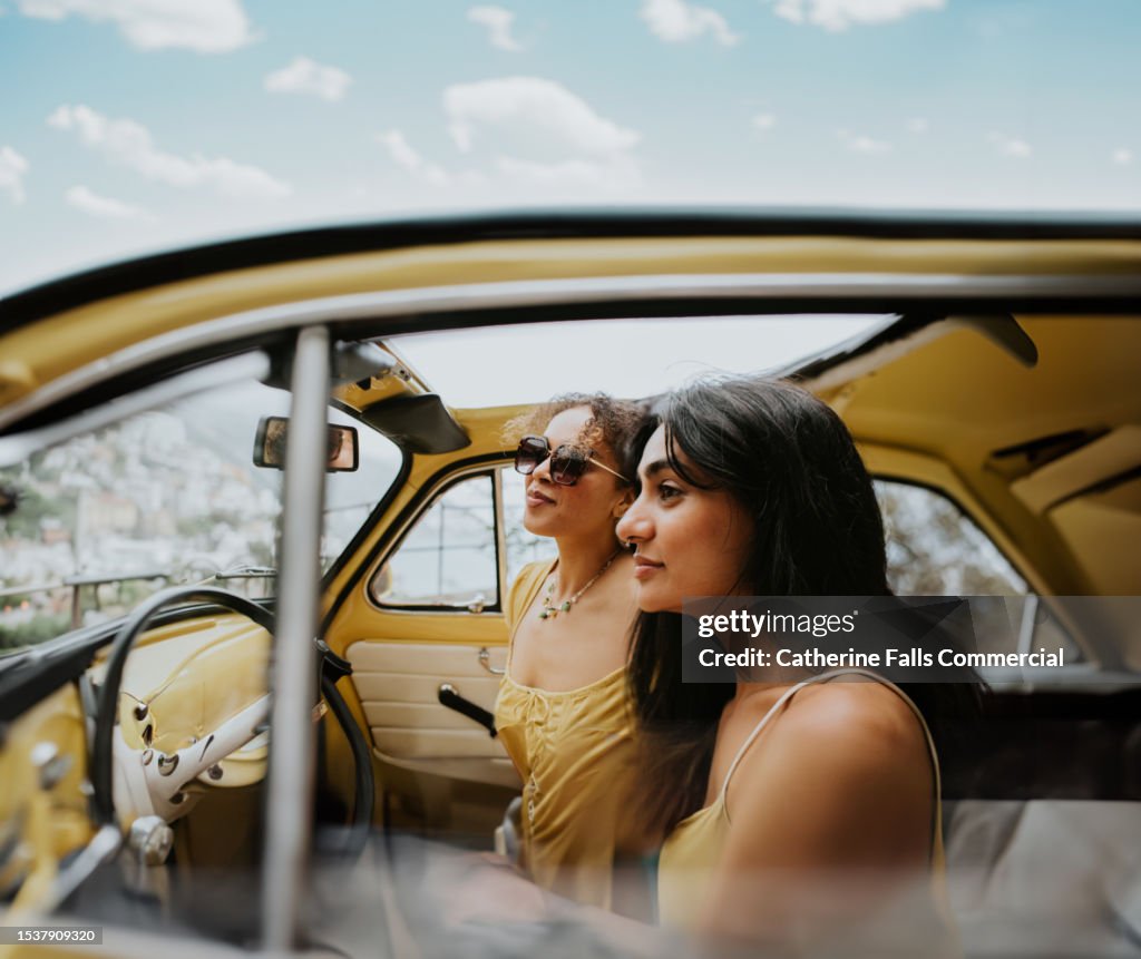 Two beautiful woman drive a vintage yellow convertible fiat