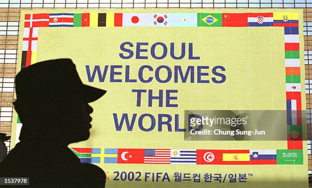 Silhouetted South Korean police officer stands guard in front of a giant banner showing the national flags of the countries that will participate in...