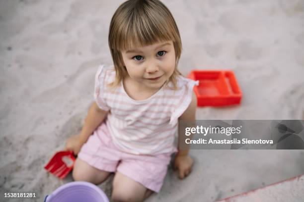 small girl playing in the sandbox, looking at camera - sandkasten stock-fotos und bilder