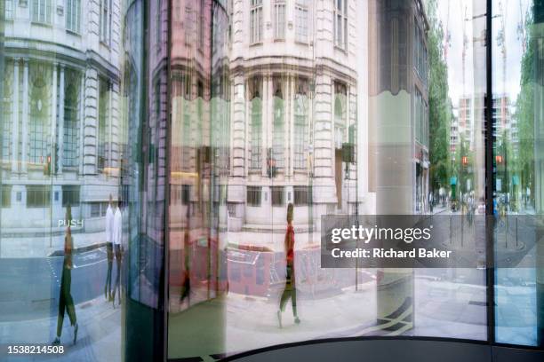 City workers are reflected and distorted in the glass entrance of an office workplace in the City of London, the capital's financial district, on...