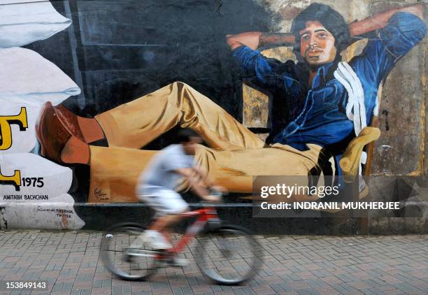 An Indian cyclist rides past a mural of Bollywood actor Amitabh Bachchan from his classic film 'Deewar' on the eve of Bachchan's 70th birthday in...