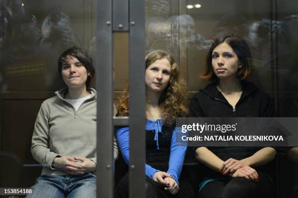 Members of the all-girl punk band "Pussy Riot" Yekaterina Samutsevich, Maria Alyokhina and Nadezhda Tolokonnikova sit in a glass-walled cage in a...