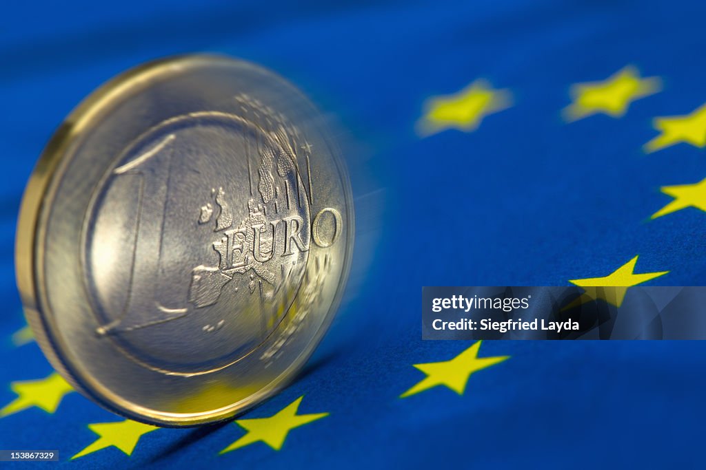 Euro coin rolling on an EU flag