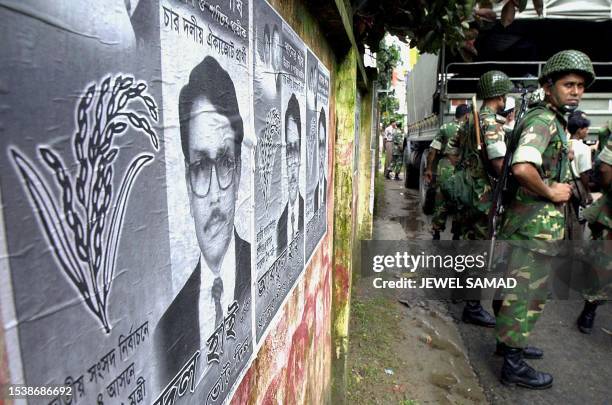 Group of Bangladeshi army troops stand guard beside an election poster promoting Bangladesh Nationalist Party member Abdul Hai on a main road in the...