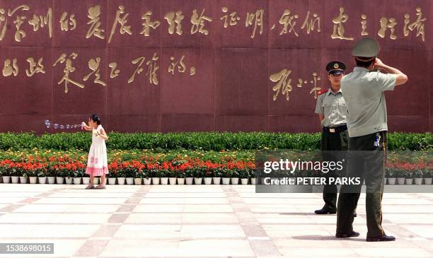 Girl blows bubbles as two PLA cadet soldiers take a picture in front of an inscription which says "Shenzhen's economic development and experience...