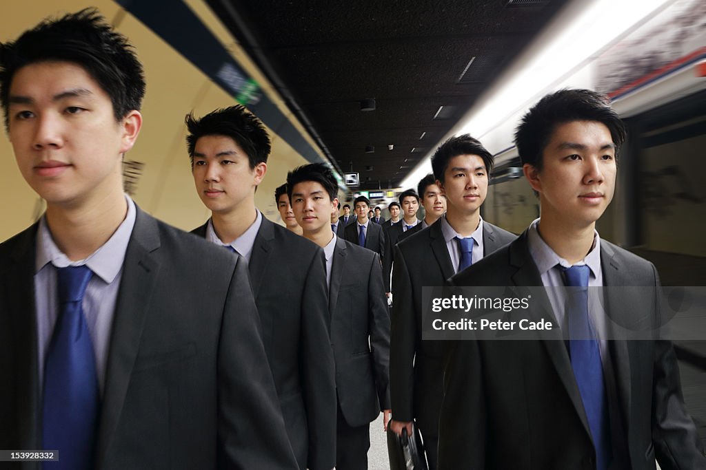 Identical men in suits walking along platform