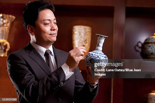 mature businessman admiring an antique chinese vase - kunsthändler stock-fotos und bilder