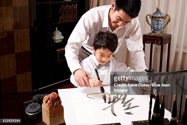 father and son practising chinese calligraphy - chinese family stock-fotos und bilder