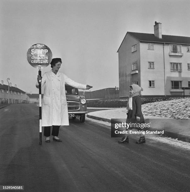 Child crossing a road with the aid of a lollipop lady at a housing estate in Swindon, Wiltshire, January 29th 1959.