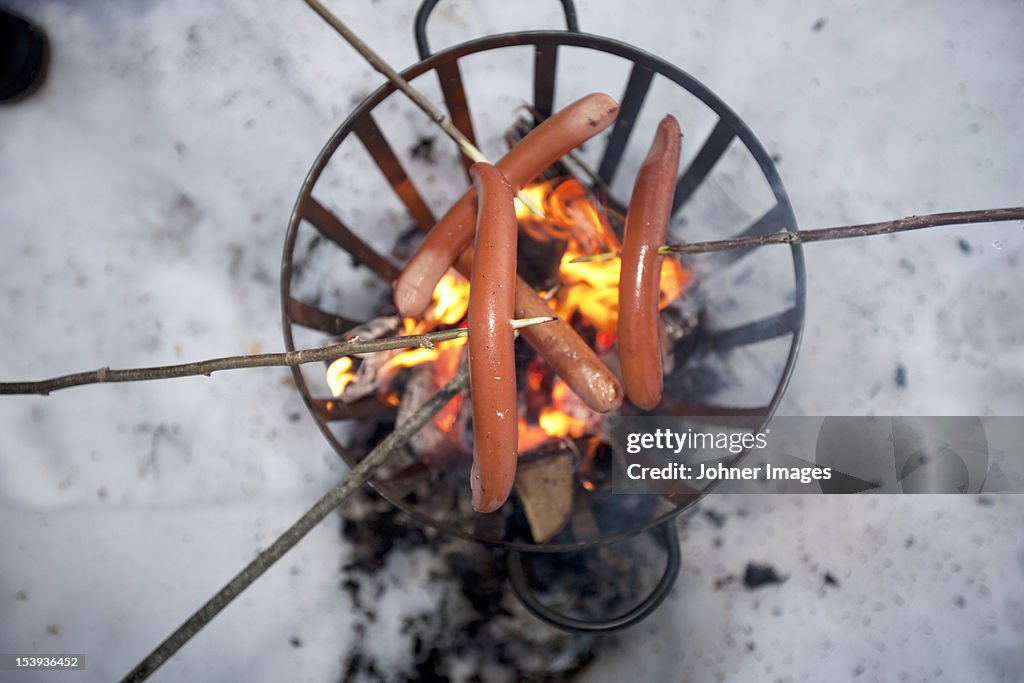 Sausages on sticks above fire