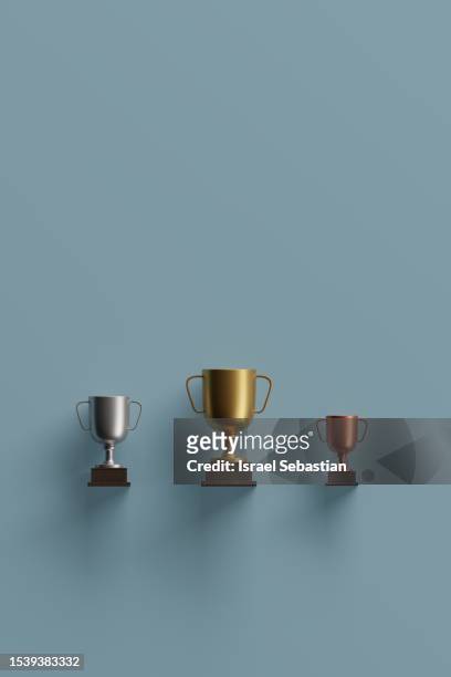 digitally generated image of gold, silver and bronze trophies on blue background. - gold patina stock pictures, royalty-free photos & images