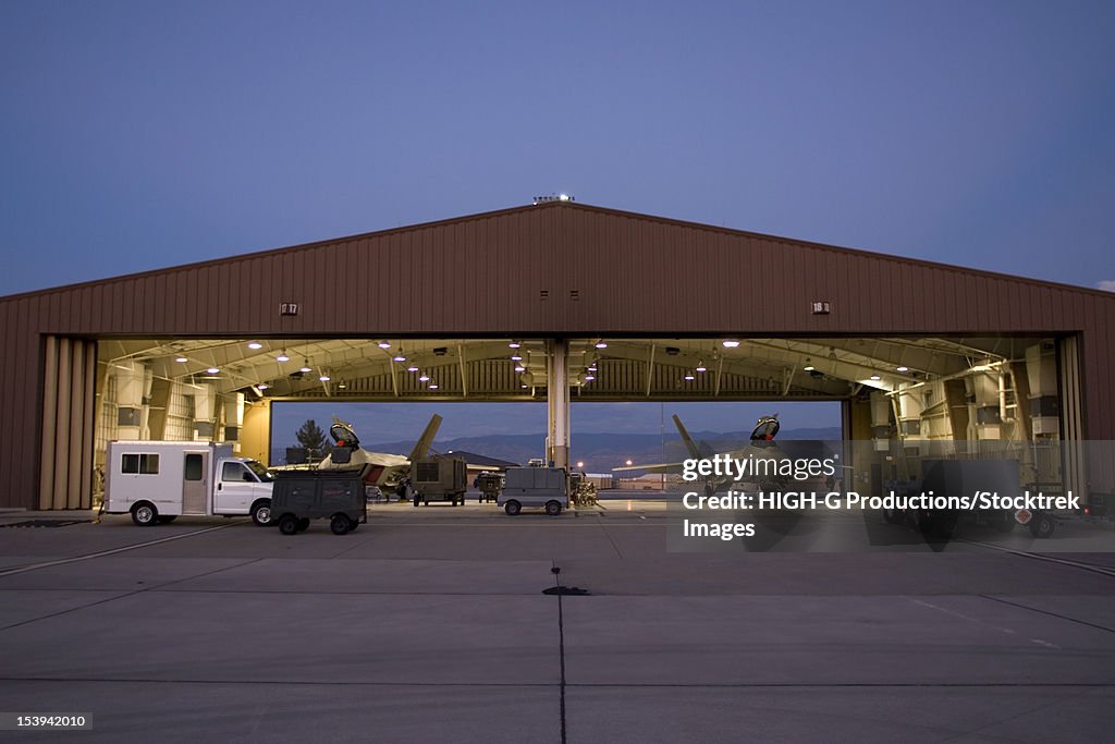 Two F-22 Raptors sit in their hangars while maintenance crews work on them between sorties at Holloman Air Force Base, New Mexico.