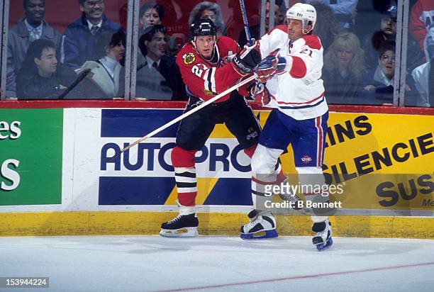 Jeremy Roenick of the Chicago Blackhawks is checked into the boards by Guy Carbonneau of the Montreal Canadiens during an NHL game circa 1990 at the...