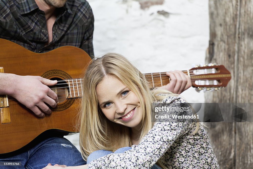 Woman smiling, man playing guitar in background