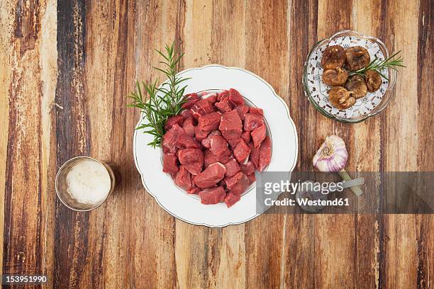 plate of raw goulash and dried figs, garlic bulbs and beer glass on wooden table - wildbret stock-fotos und bilder