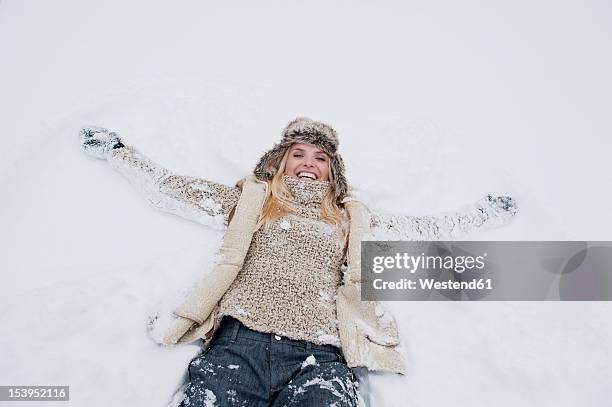 austria, salzburg county, mid adult woman lying on snow, smiling - women winter snow stock-fotos und bilder