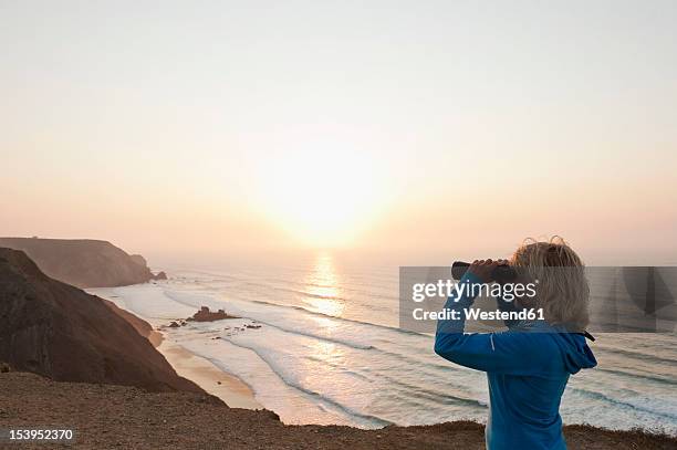 portugal, algarve, sagres, senior woman looking at beach through binocular - looking through binoculars stock pictures, royalty-free photos & images