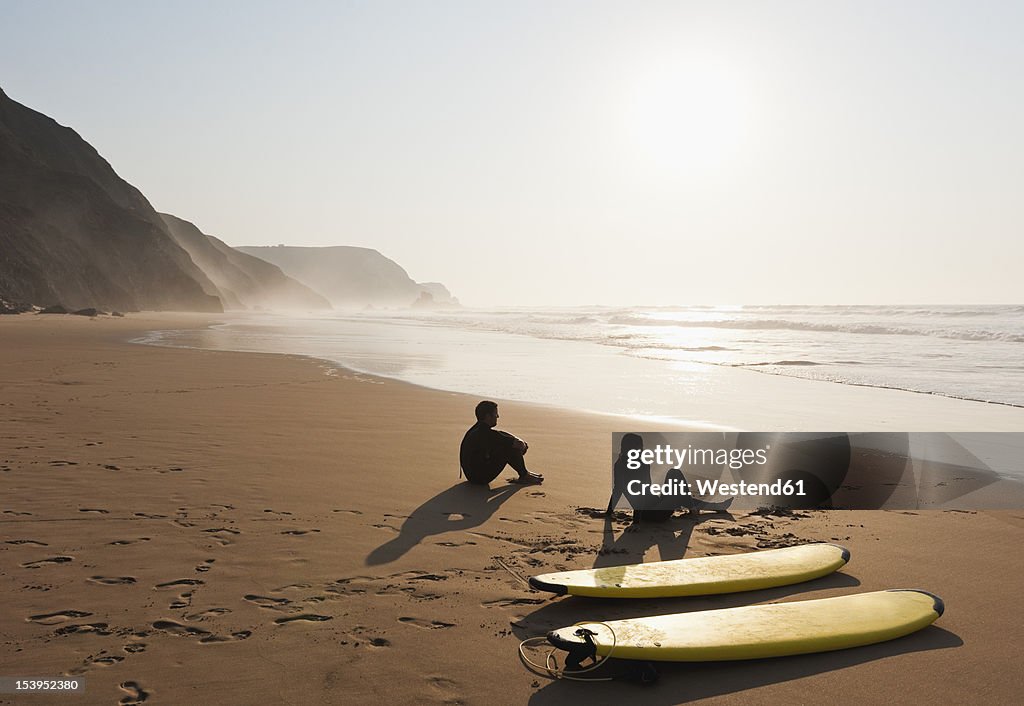Portugal, Couple sitting on beach by surfboard