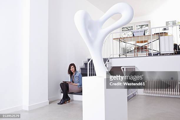 germany, cologne, mid adult woman sitting on stairs in art gallery, portrait - skulptur kunstwerk stock-fotos und bilder