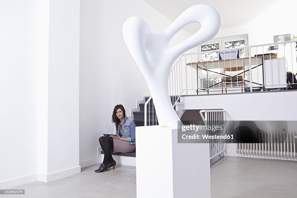 Germany, Cologne, Mid adult woman sitting on stairs in art gallery, portrait